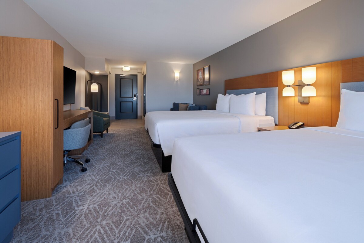 A hotel room with two beds, a desk with a chair, a wardrobe, and a bathroom door.