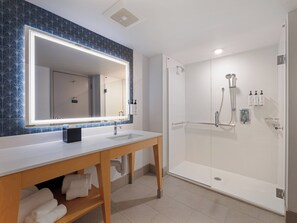 A modern bathroom with a large mirror, a shower, and a vanity with towels.