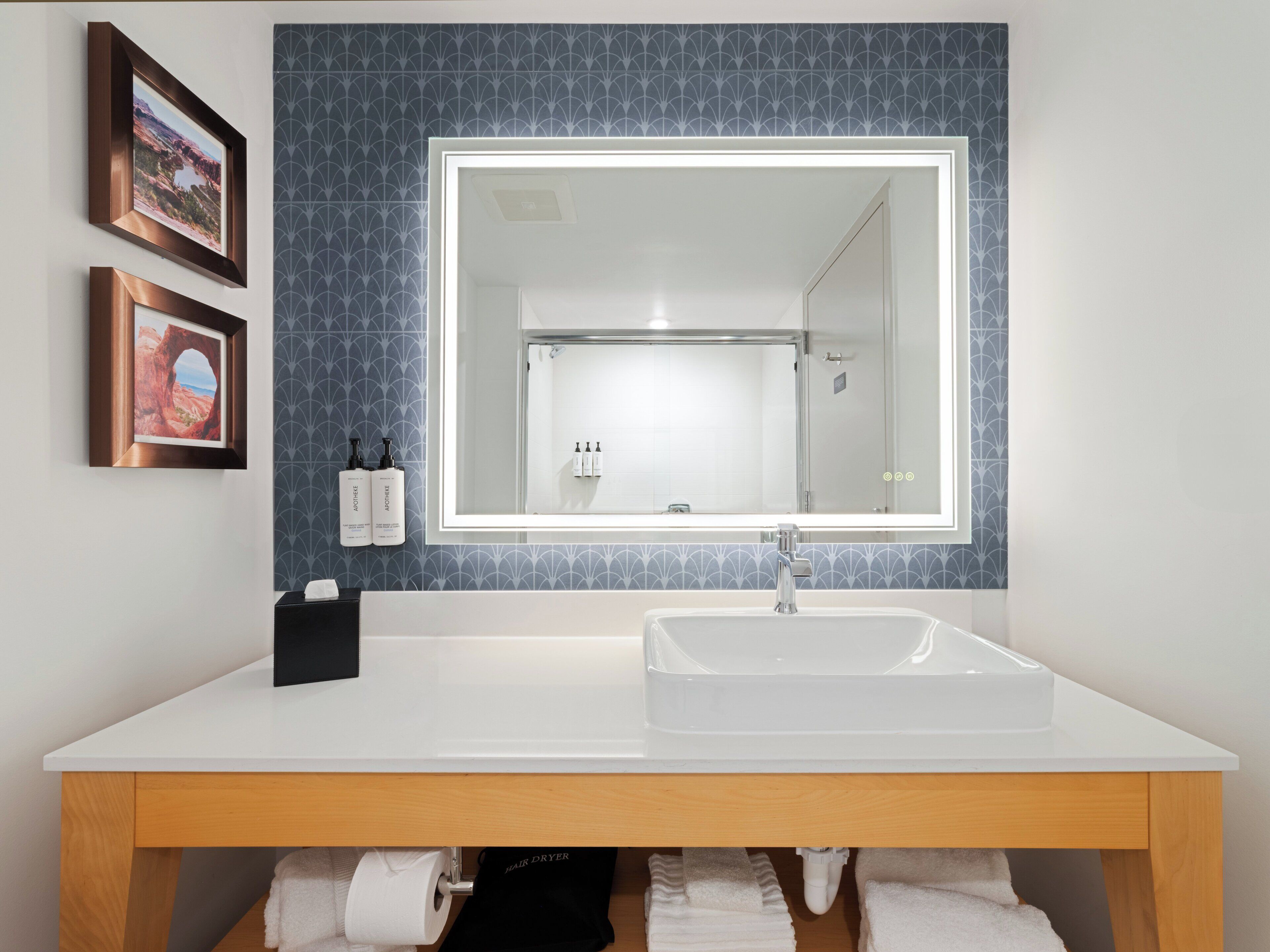 A modern bathroom with a large mirror, white sink, and two framed pictures on the wall.