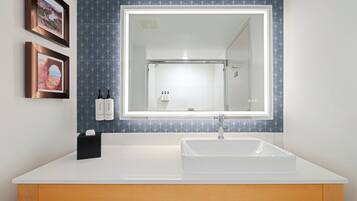 A modern bathroom with a large mirror, white sink, and two framed pictures on the wall.