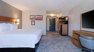 A hotel room with a large bed, a desk, a chair, a wardrobe, and a television.
