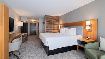 Una habitación de hotel con una cama grande, un escritorio con silla, un pequeño sofá, un televisor y una lámpara de pared.