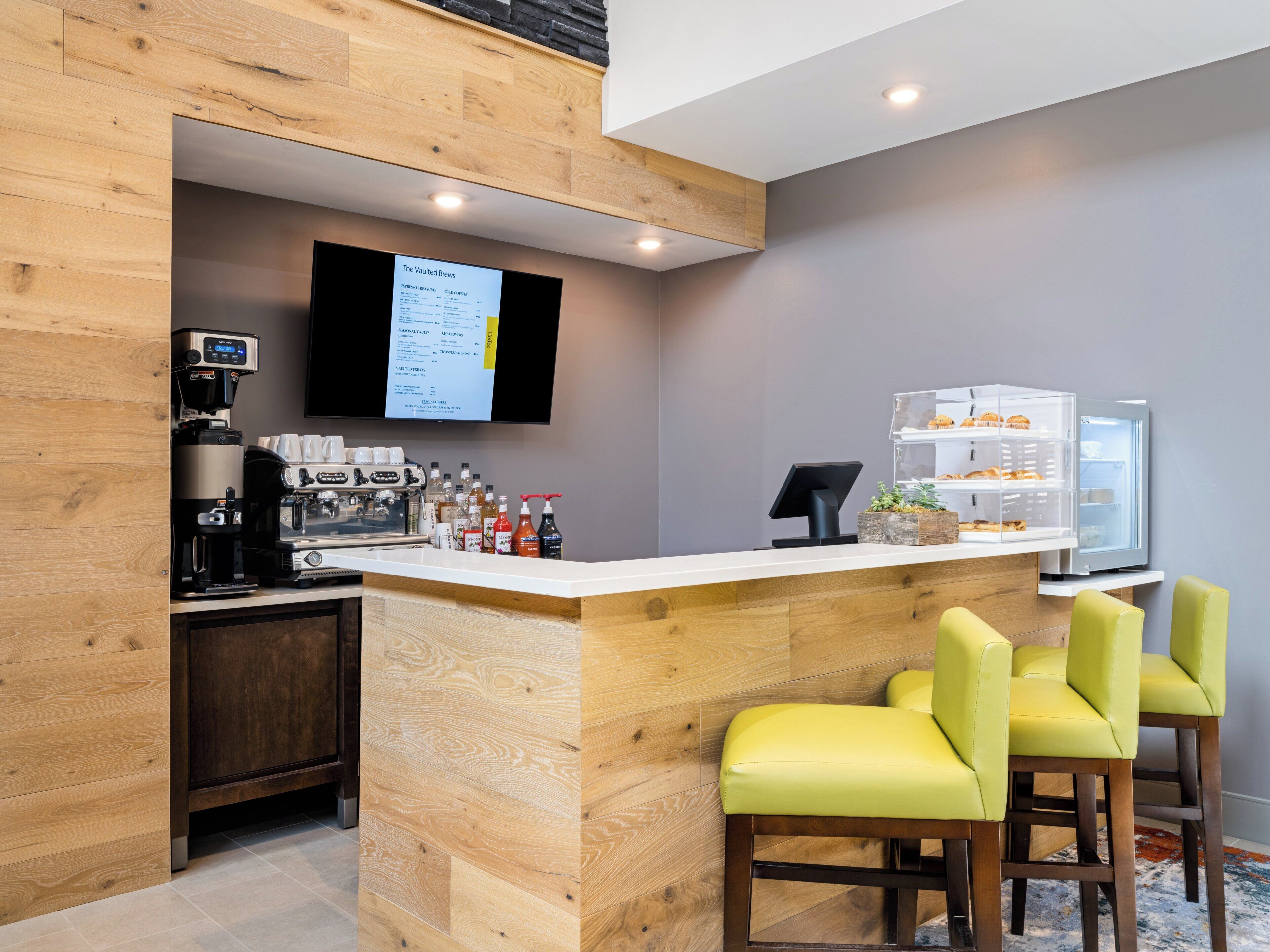 Un espace bar moderne avec un comptoir en bois, une machine à café et un tableau affichant le menu.