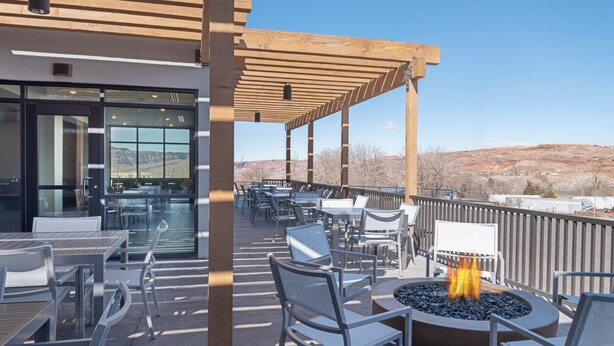 An outdoor patio with tables and chairs, a fire pit, and a view of the mountains. - voco Moab by IHG (Moab)