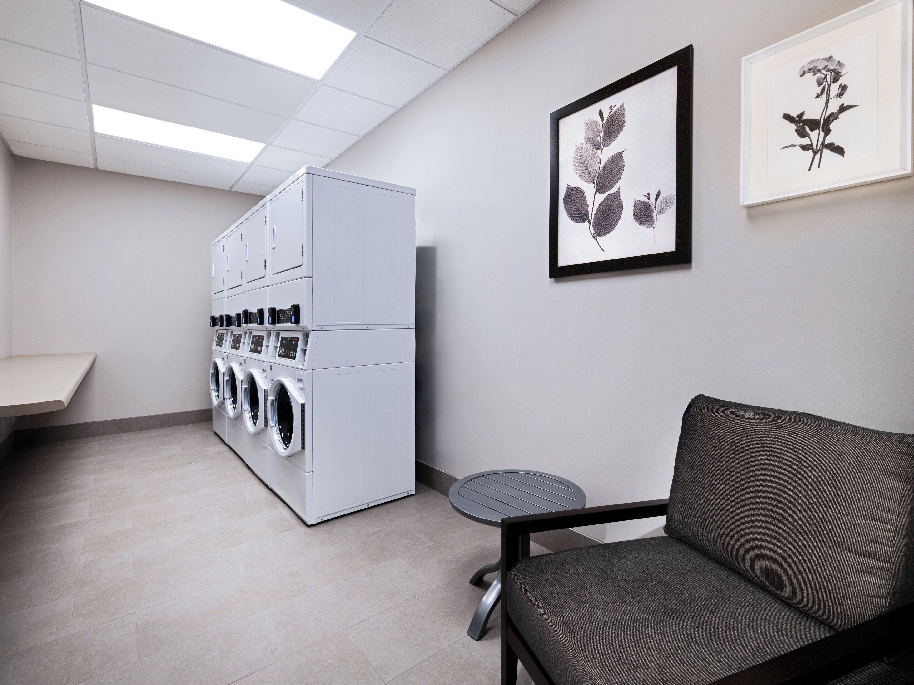A laundry room with a large washer and dryer, a small table, and two framed botanical prints on the wall.