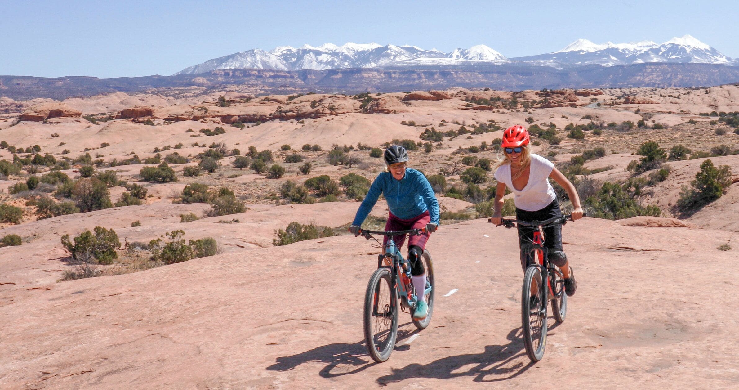 Two people riding bicycles on a rocky terrain with a mountain range in the background.