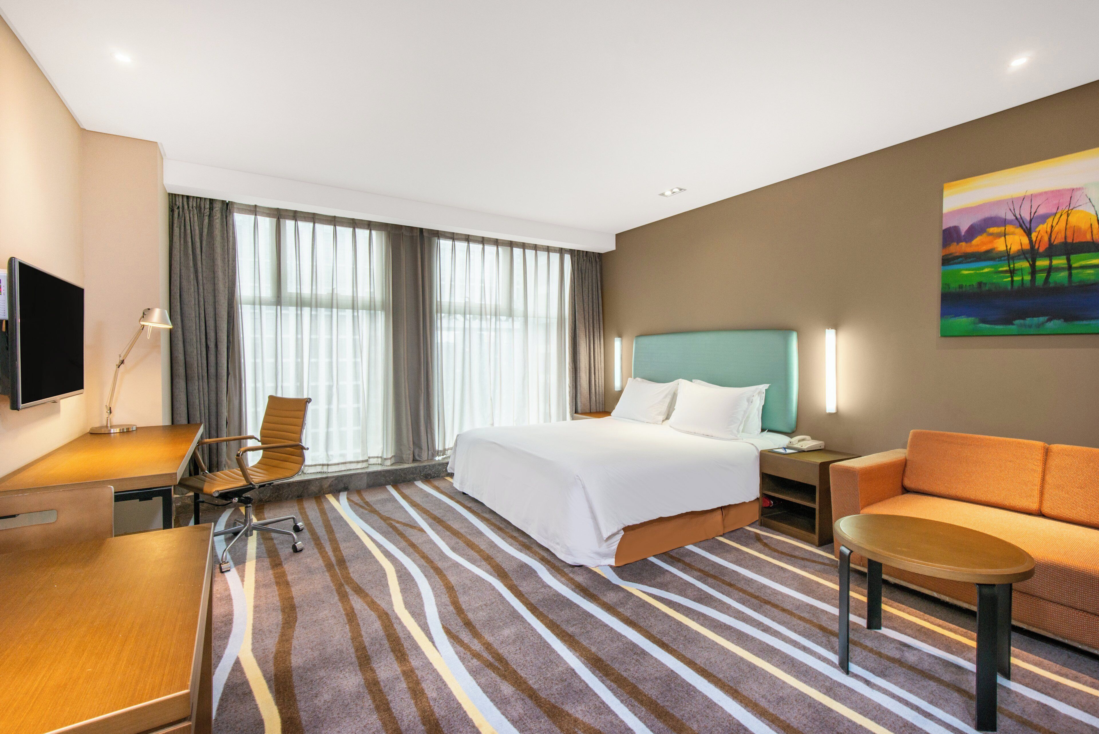 Ein Hotelzimmer mit Bett, Schreibtisch, Stuhl, Sofa, Fernseher und einem Bild an der Wand.