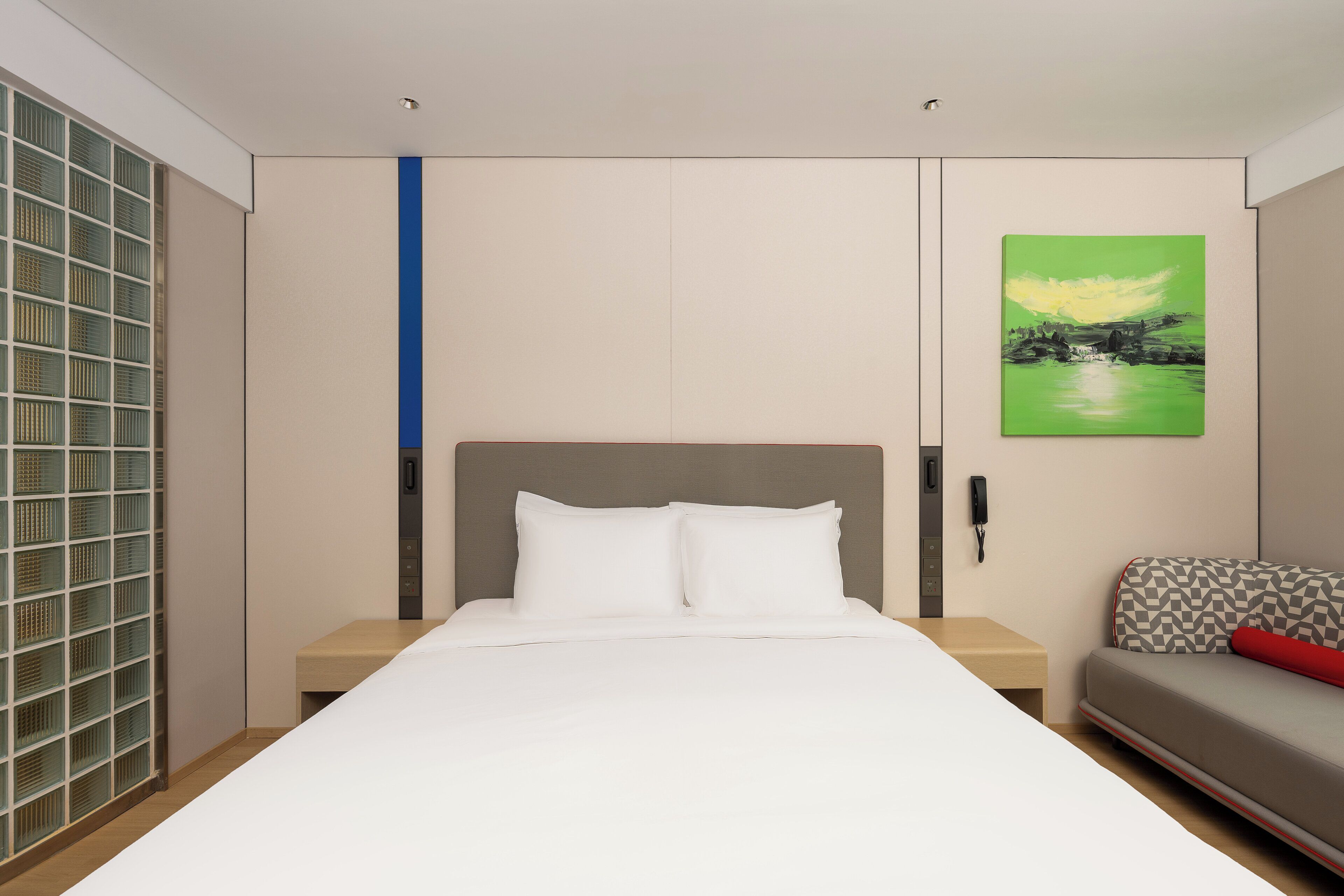 A hotel room with a bed, a bedside table, a phone, a painting, and a sofa.