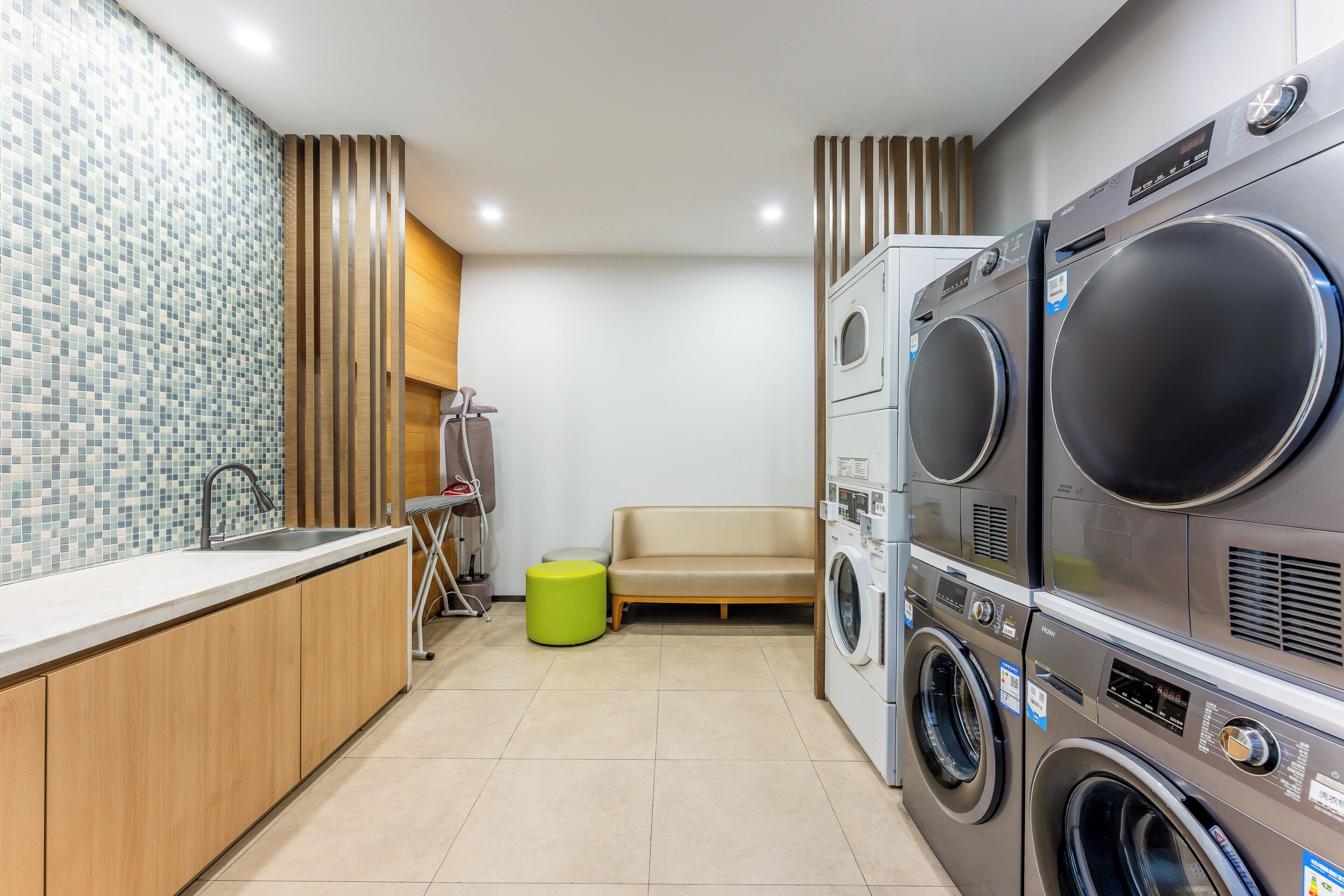 A laundry room with two stacked washing machines, a bench, and a small table with a hose.