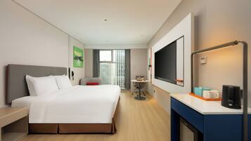 A modern hotel room with a large bed, a desk with a coffee maker, a TV, and a window with a city view.