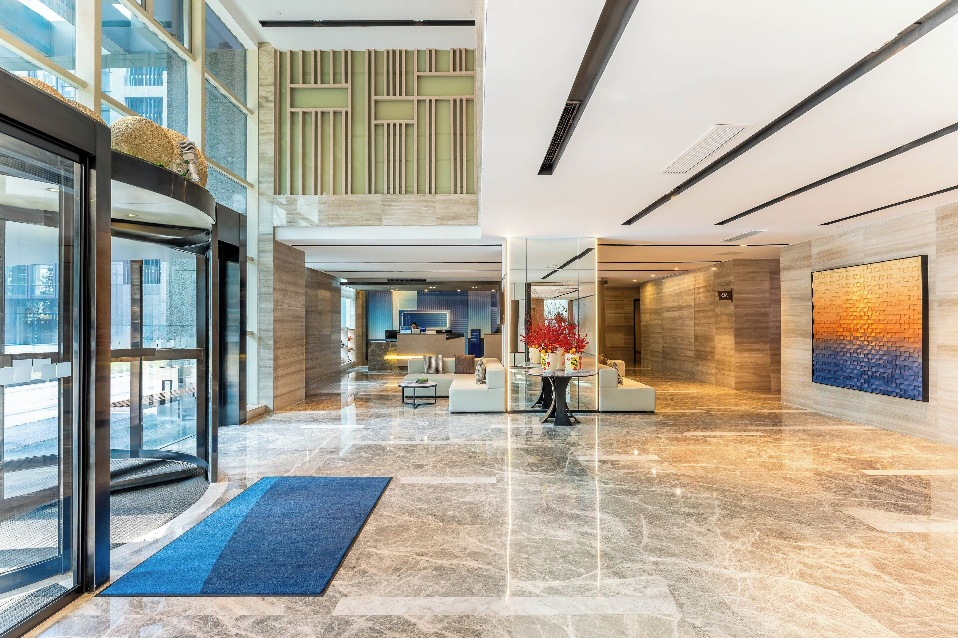 A modern hotel lobby with a reception desk, seating area, and a large window overlooking the city.