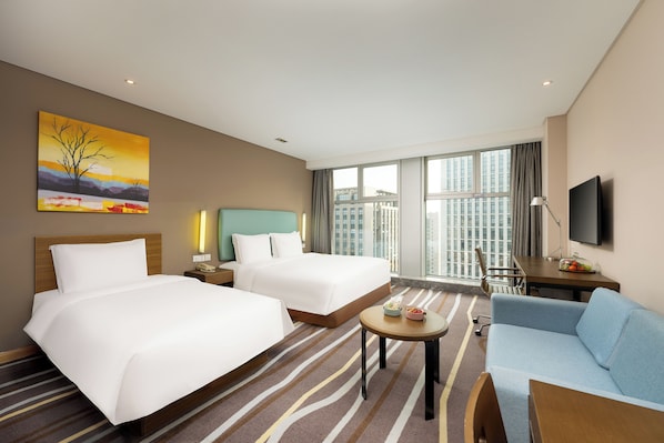 Habitación de hotel con dos camas, un sofá, un escritorio, un televisor y un ventanal con vistas a la ciudad.