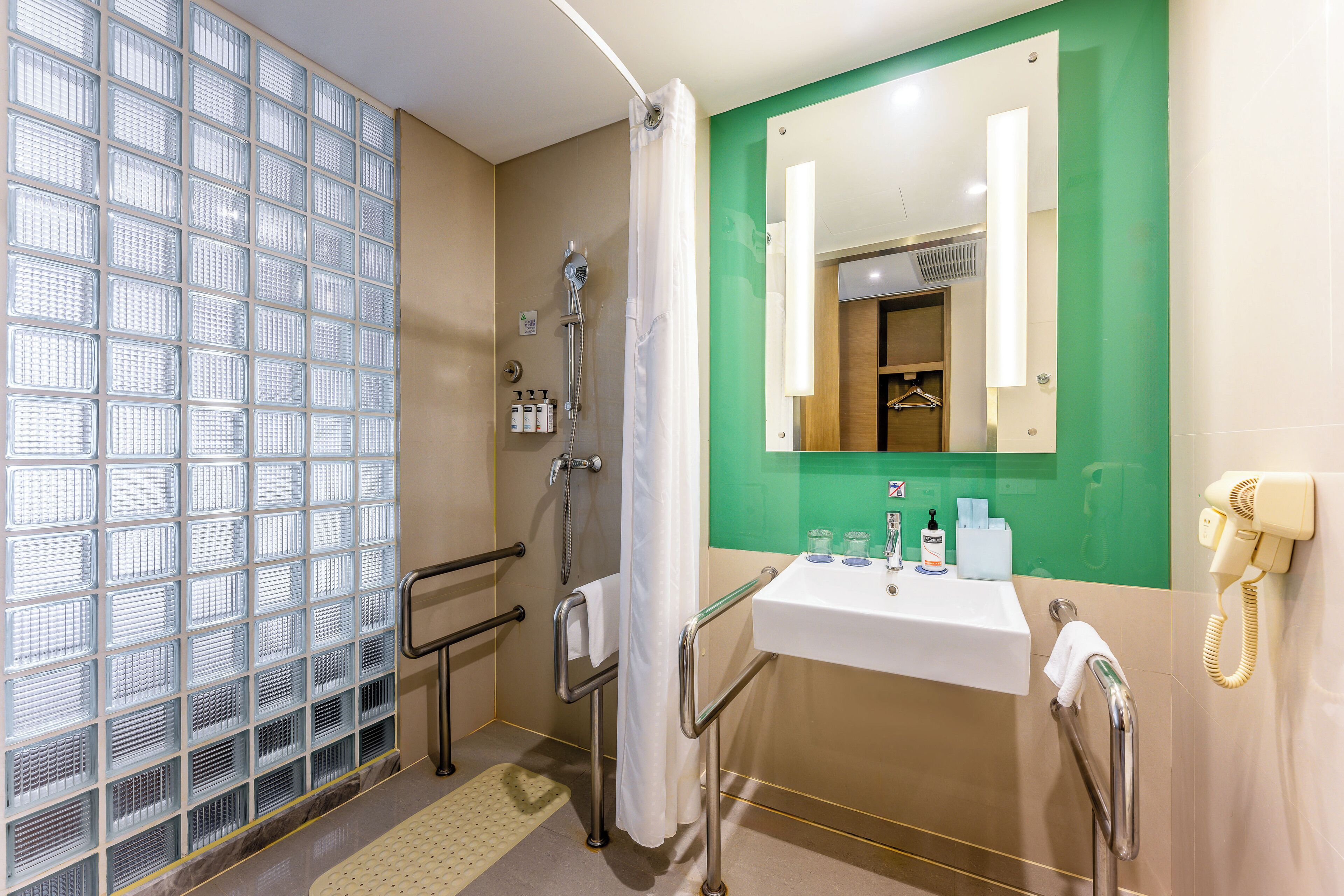 A bathroom with a shower, a sink, a mirror, and a telephone.