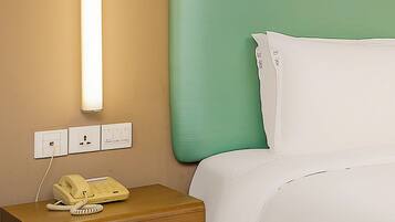 Habitación de hotel con mesita de noche de madera, teléfono amarillo, pared verde y ropa de cama blanca.
