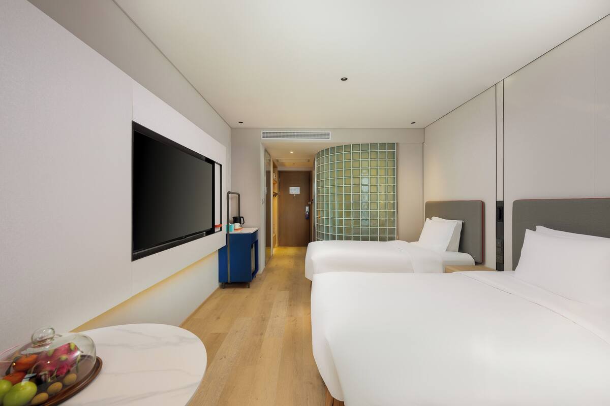 Quarto de hotel com duas camas, televisão, minibar e banheiro visível por uma porta aberta.