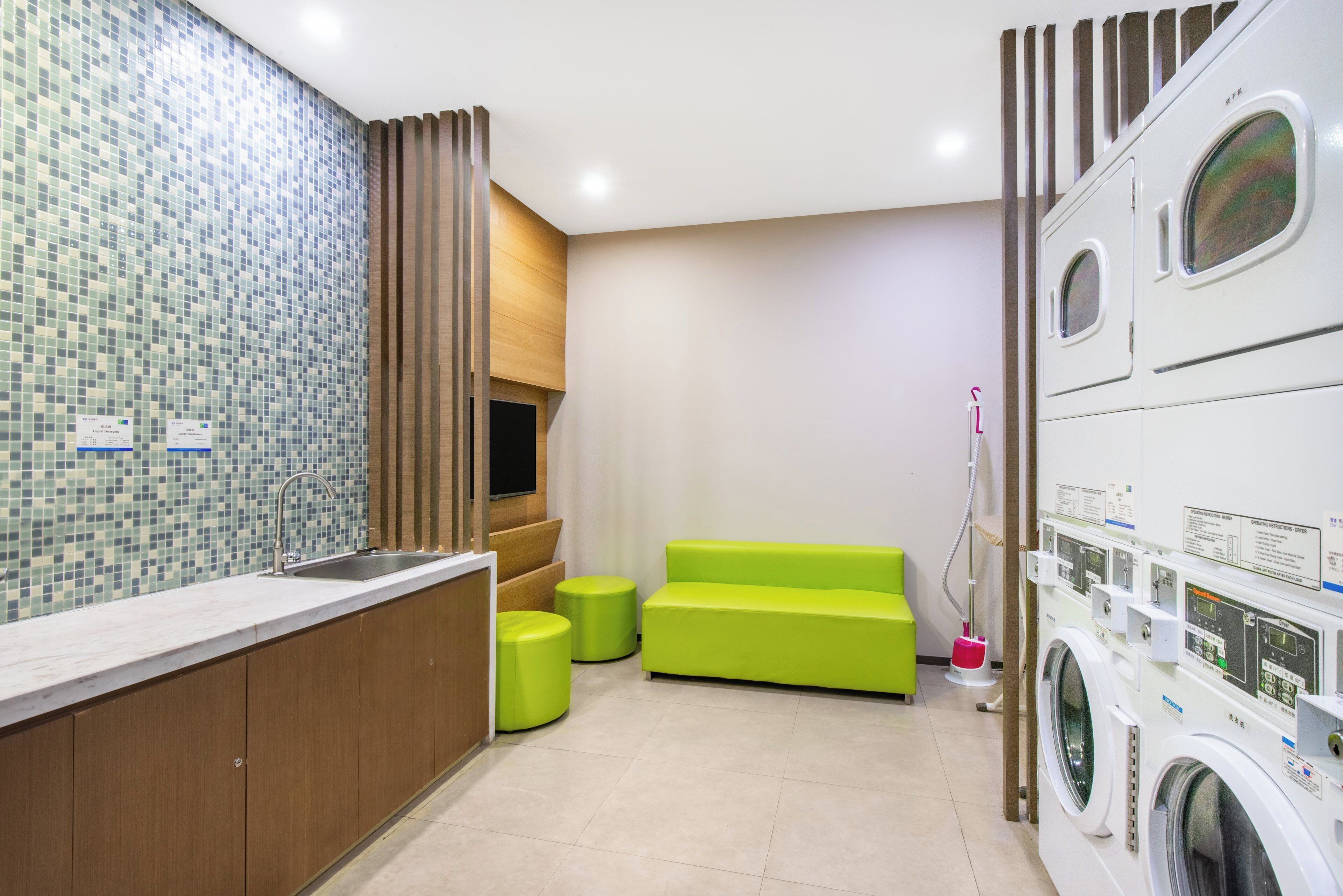 Une chambre d’hôtel avec un mur recouvert de carreaux, un lambris en bois, un lavabo, un canapé vert et un lave-linge.