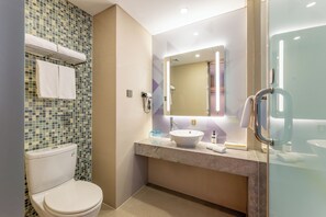 Un baño moderno con inodoro, lavamanos con un espejo grande y cabina de ducha de vidrio.