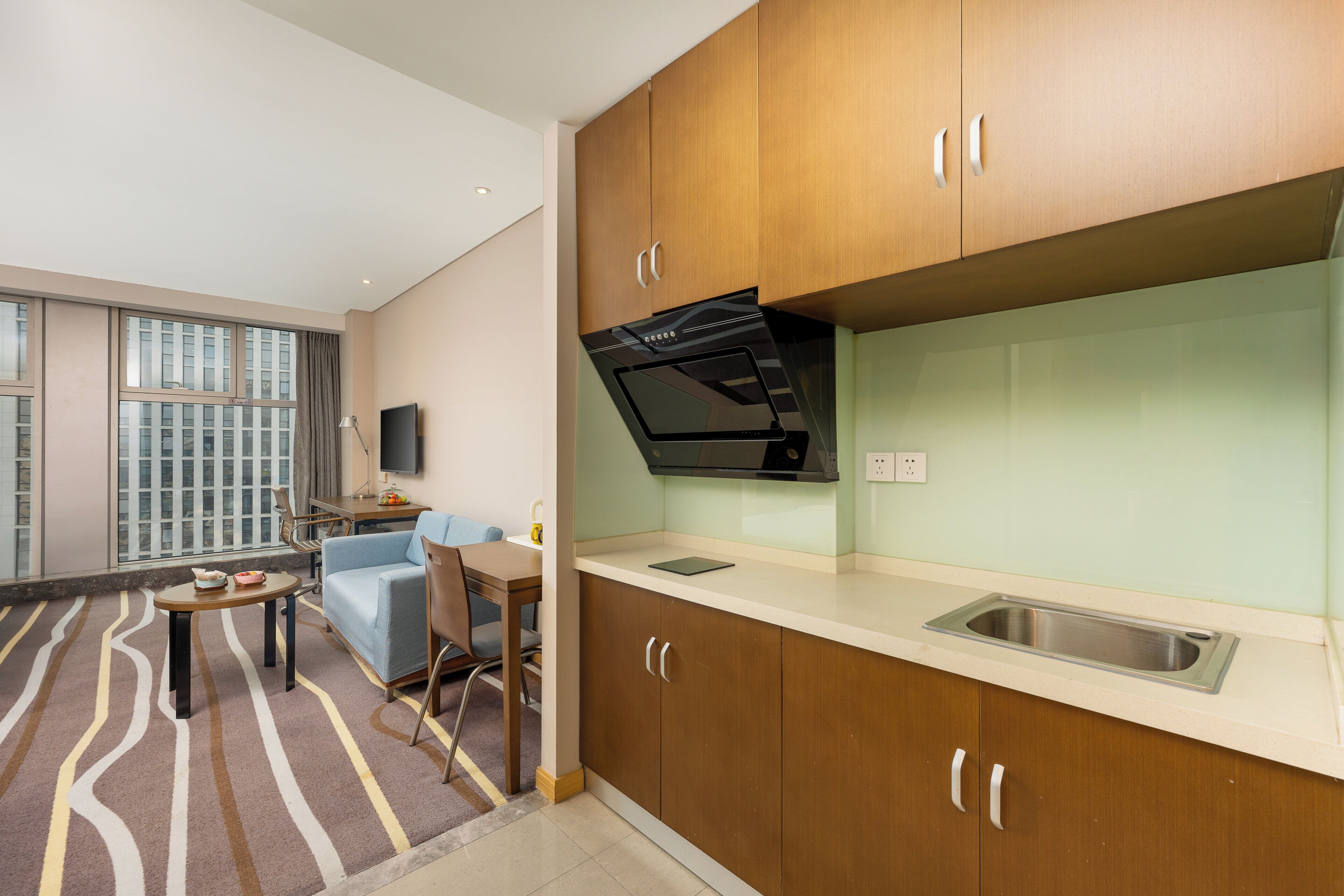 A modern kitchen with wooden cabinets, a built-in oven, and a window overlooking a cityscape.