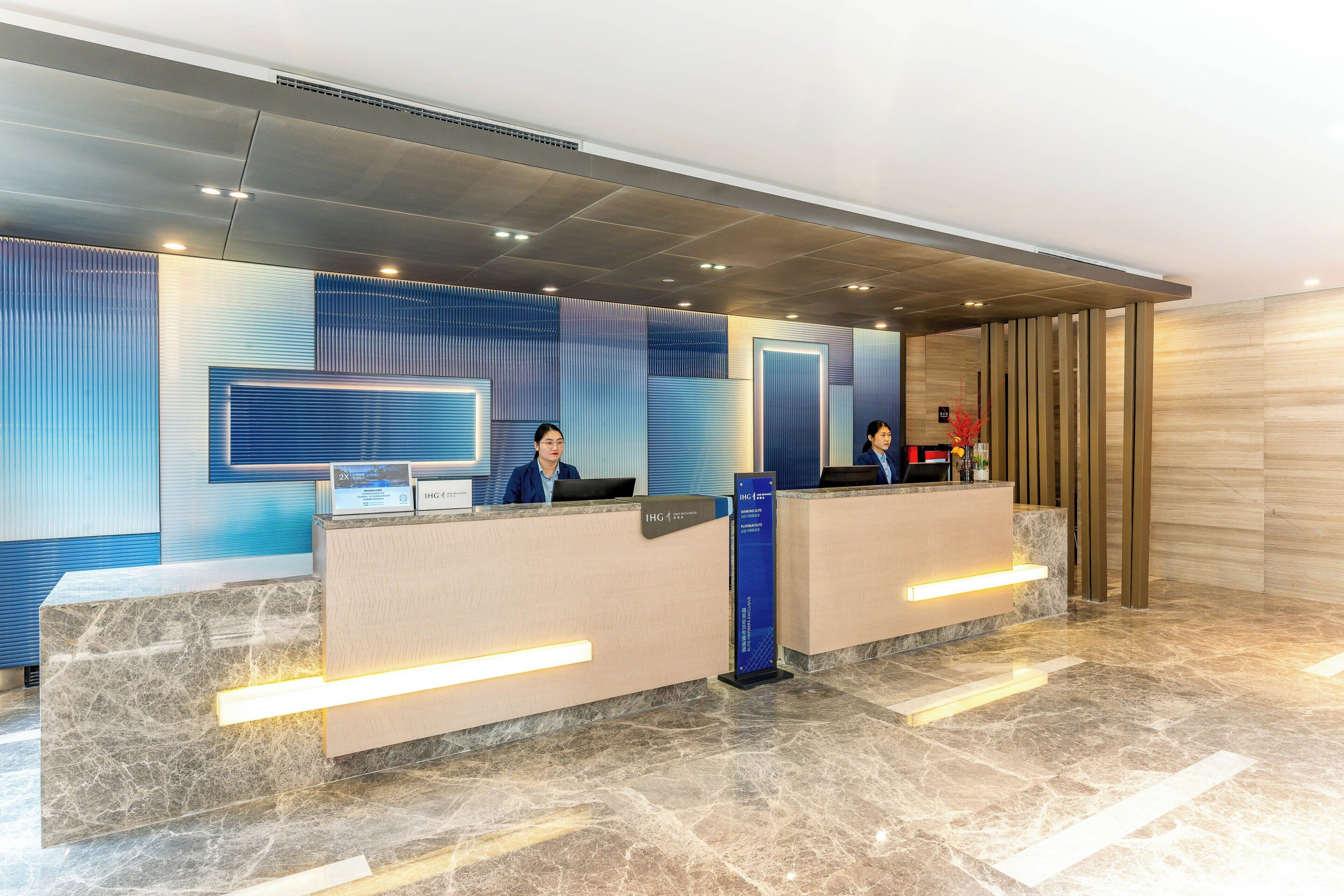 Uma área de recepção de hotel com dois balcões, uma grande tela digital e design de interiores moderno.