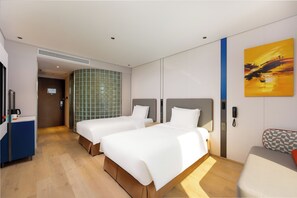 Habitación de hotel con dos camas, un escritorio, una silla, un cuadro y la puerta del baño.