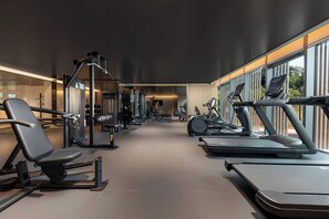 Une salle de sport moderne équipée de divers appareils d’exercice, notamment des tapis de course et des appareils de musculation, et dotée de grandes fenêtres qui laissent entrer la lumière naturelle.