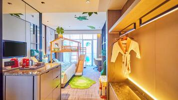 A modern hotel room with a kitchen area, a small play area with a slide, and a large window providing natural light.