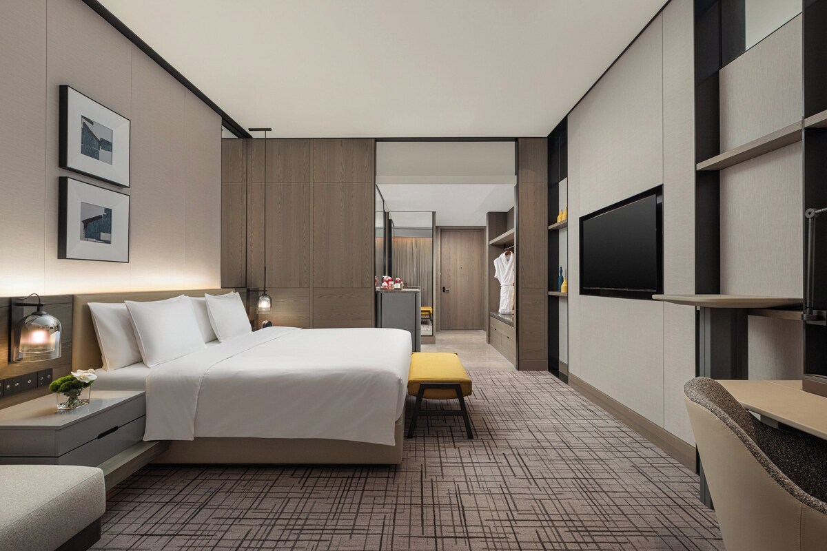 A modern hotel room with a large bed, bedside tables, a flat-screen TV, and a small seating area.