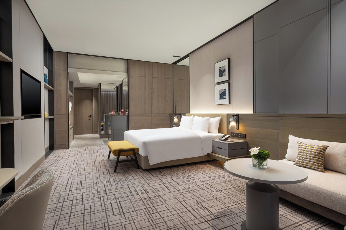 A modern hotel room with a large bed, a sofa, a small table, and a TV.
