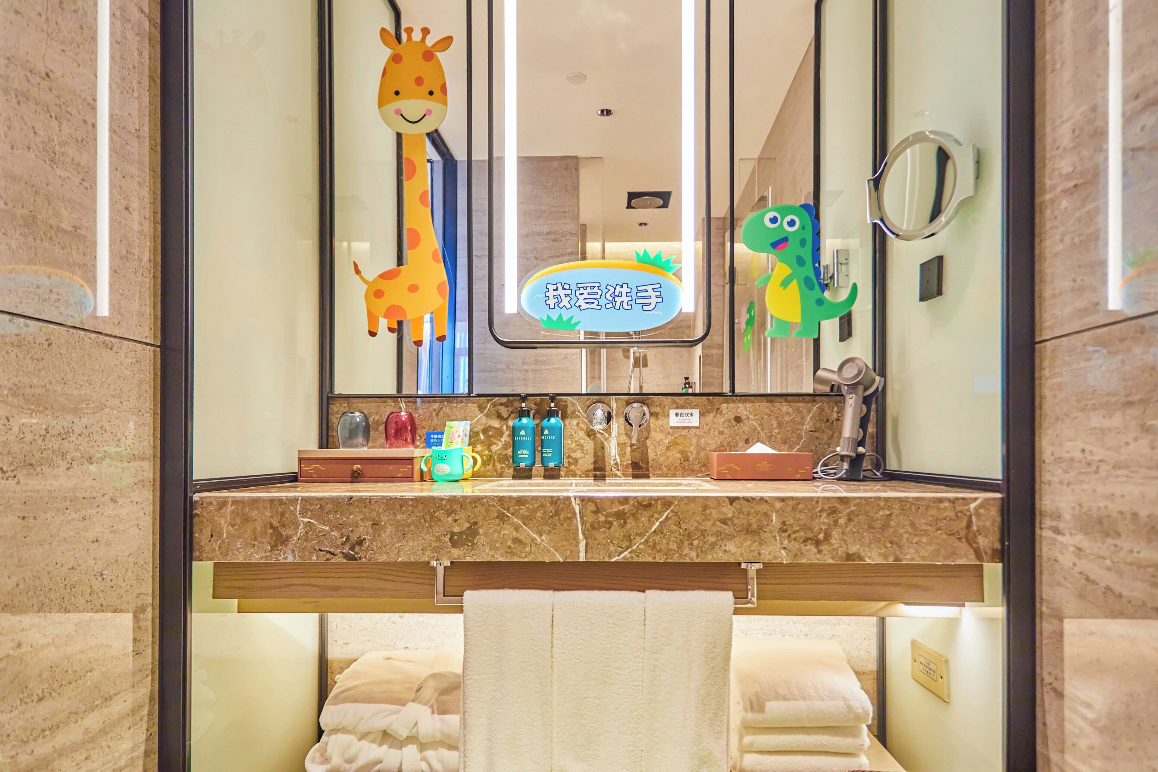 Casa de banho com bancada de mármore, espelho, porta-toalhas e área de recreação infantil decorada com animais.