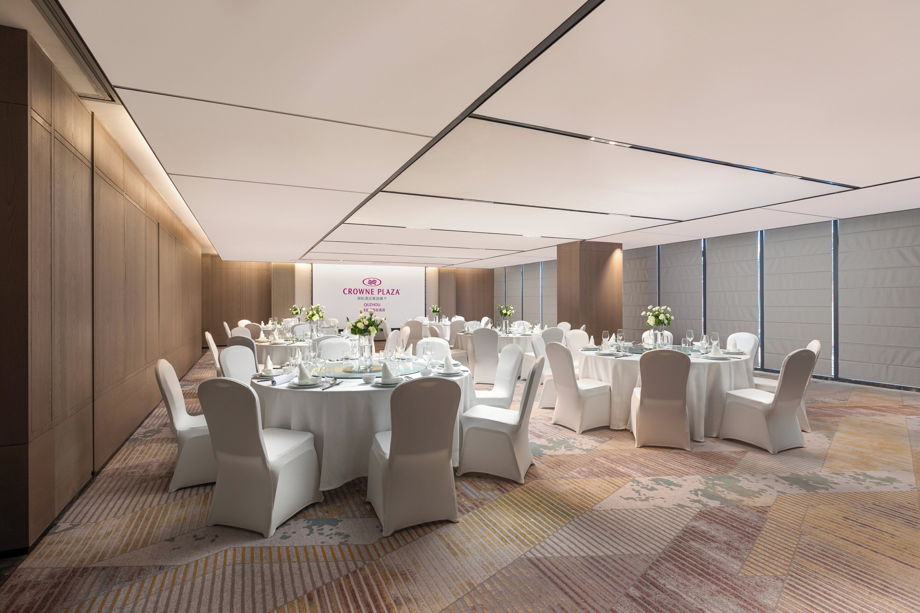 A conference room with round tables, white chairs, and a banner reading "CROWNE PLAZA".