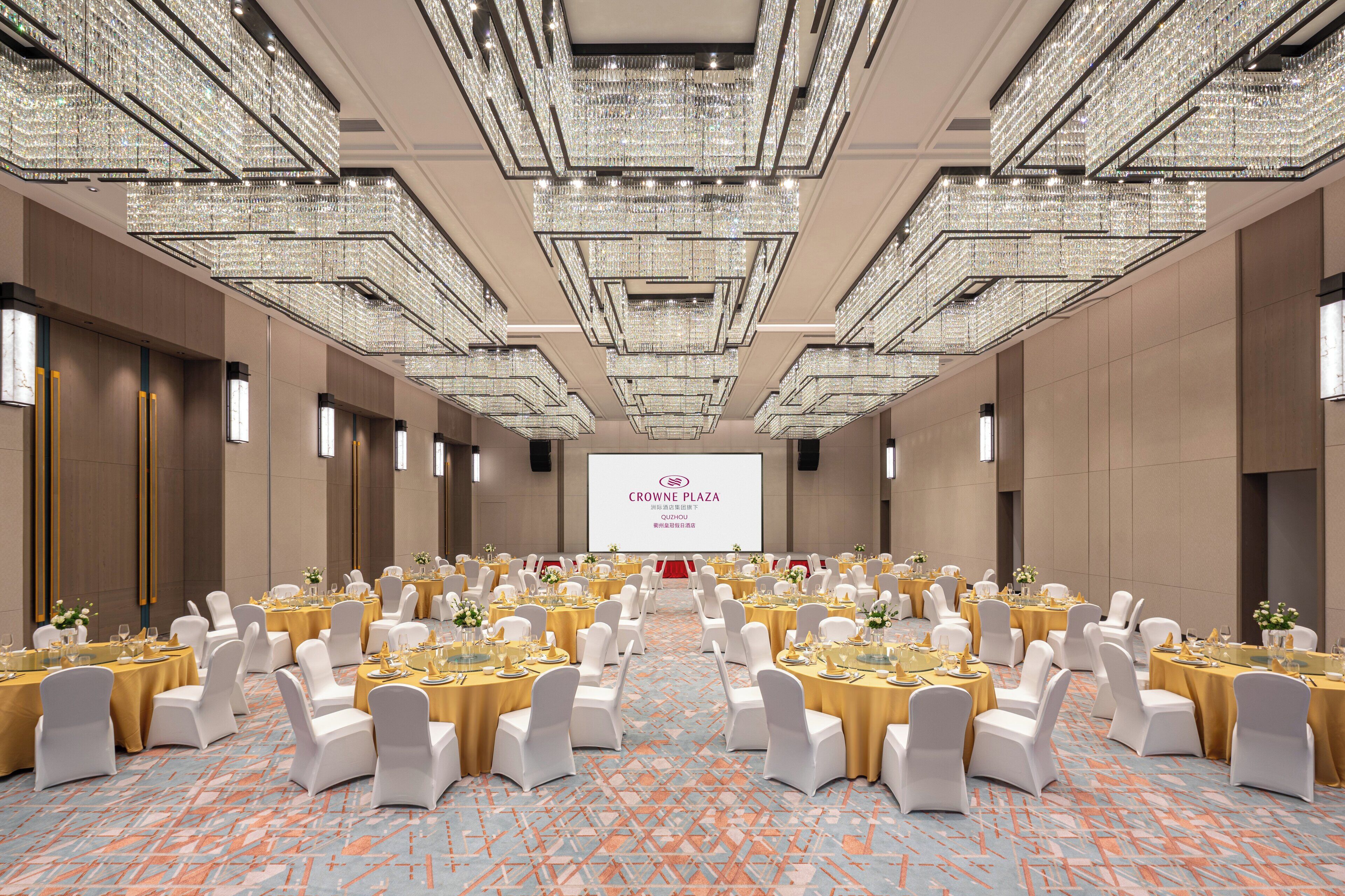 A large conference room with rows of round tables, white chairs, and a large screen at the front.