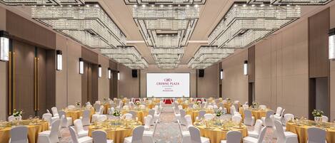 A large conference room with rows of round tables, white chairs, and a large screen at the front.