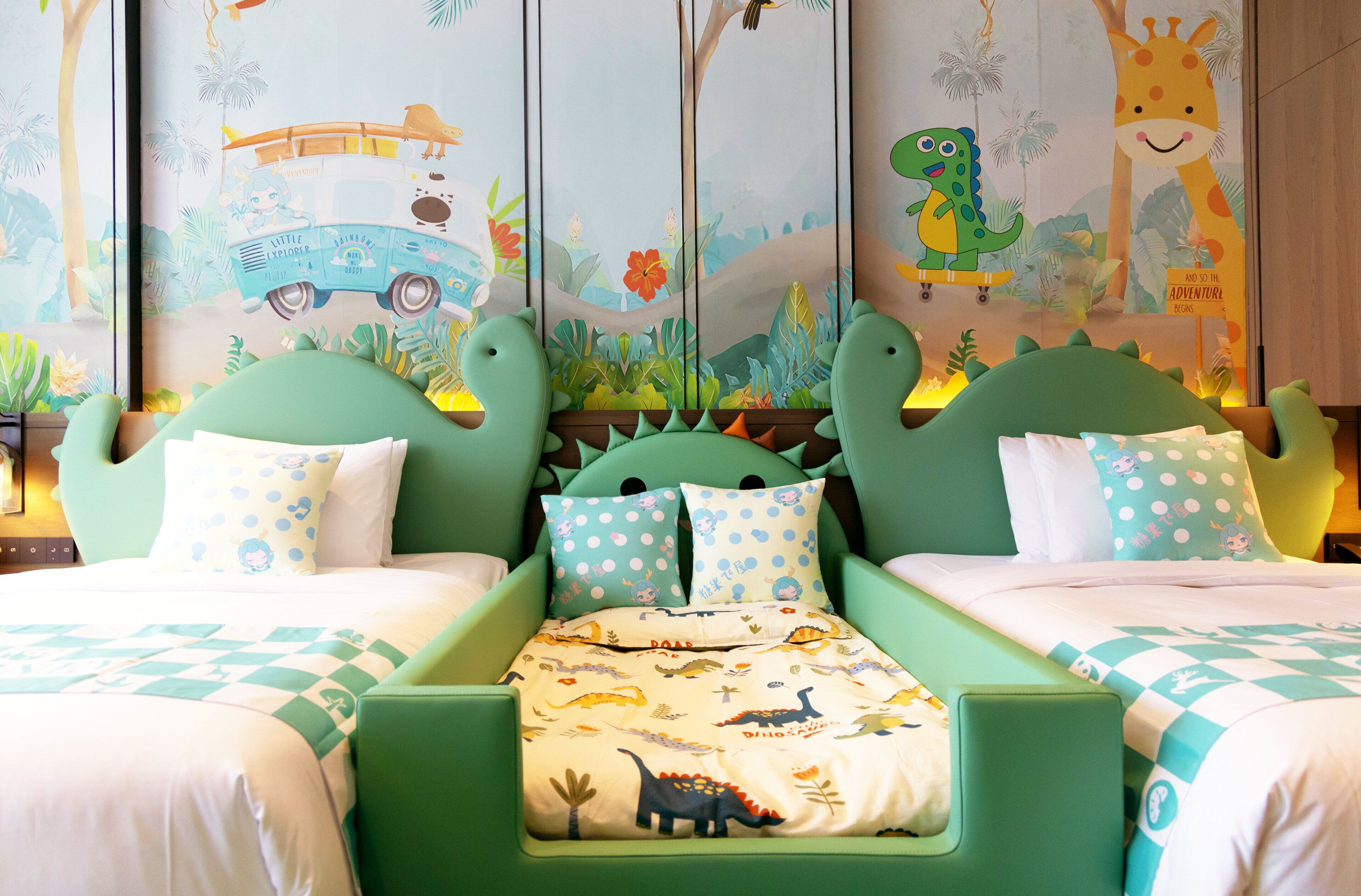 Habitación infantil con una cama verde, dos almohadas, un edredón con temática de dinosaurios y un mural con ilustraciones de jungla y animales.