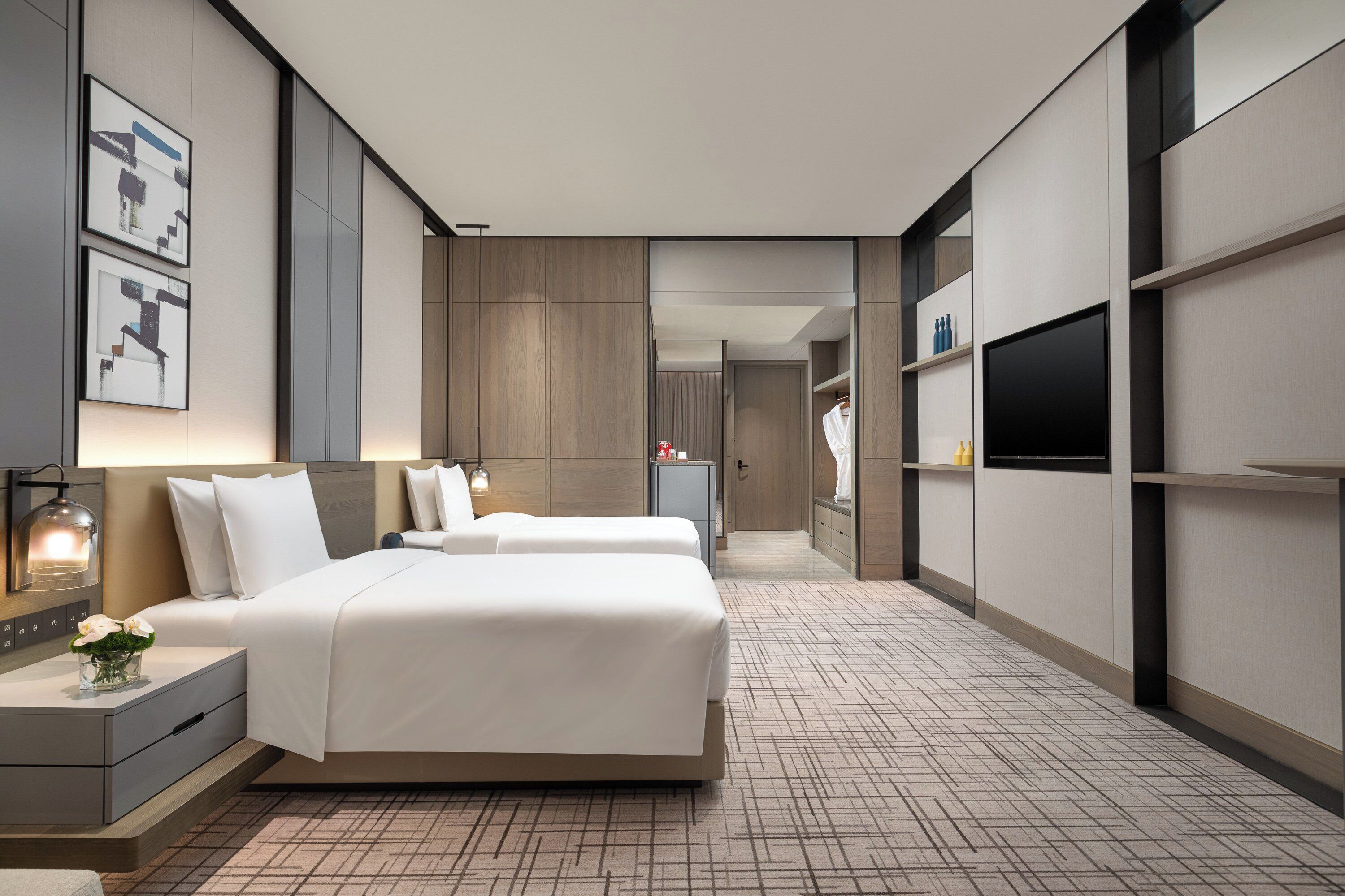 A modern hotel room with a large bed, bedside tables, a flat-screen TV, and a wardrobe.