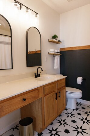 A bathroom with a white sink, wooden vanity, black and white star-patterned floor, a white toilet, and a mirror with lights above. - "The Dawning House" - Peaceful Modern Stay w/ Yard (Georgetown)