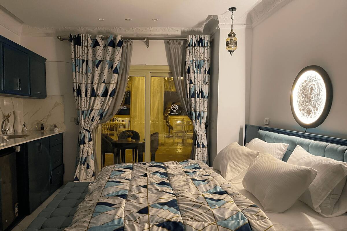 Une chambre à coucher avec un lit, des rideaux, une table de chevet et un luminaire fixé au mur.