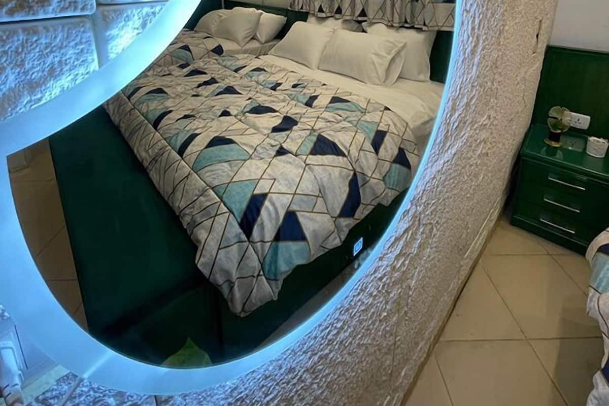 Une pièce circulaire avec un lit placé au centre, une fenêtre ronde et une table de chevet verte.