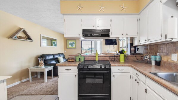 A compact kitchen with white cabinets, a black stove, and a small dining area with a black leather couch.