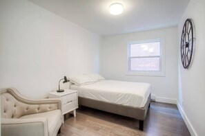 Cozy bedroom with a single bed, nightstand, and window offering a view of a nearby building.