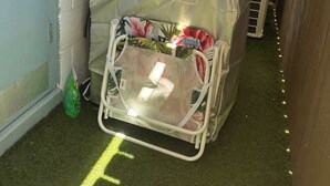 A small, enclosed space with a bed covered in a protective sheet, a green bag on the floor, and a yellow line marking on the floor. - Delightful One Bedroom Honolulu Sanctuary Renovated w/ Aircon (Honolulu)