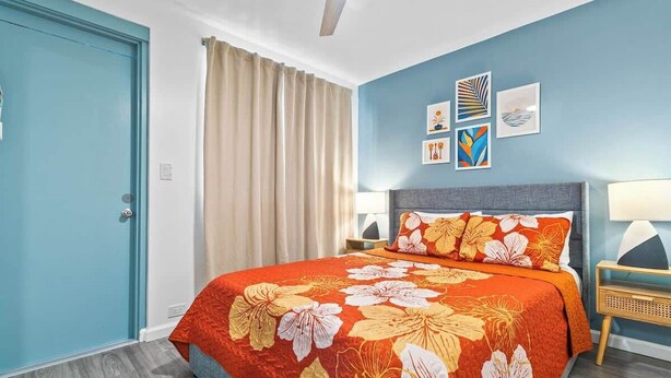 A bedroom with a bed, two bedside tables, a ceiling fan, and a window with curtains. - Delightful One Bedroom Honolulu Sanctuary Renovated w/ Aircon (Honolulu)