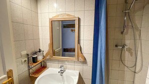 Een badkamer met een wastafel, spiegel, douche en betegelde wanden.