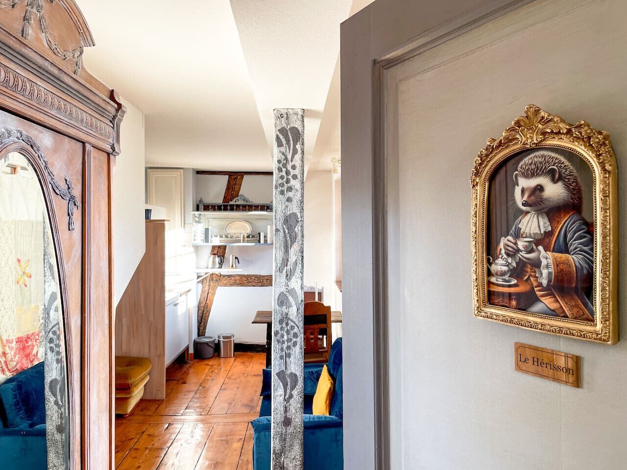 Une pièce avec un plancher en bois, un canapé bleu, un mur blanc orné d’un tableau encadré et un escalier menant à une autre pièce.