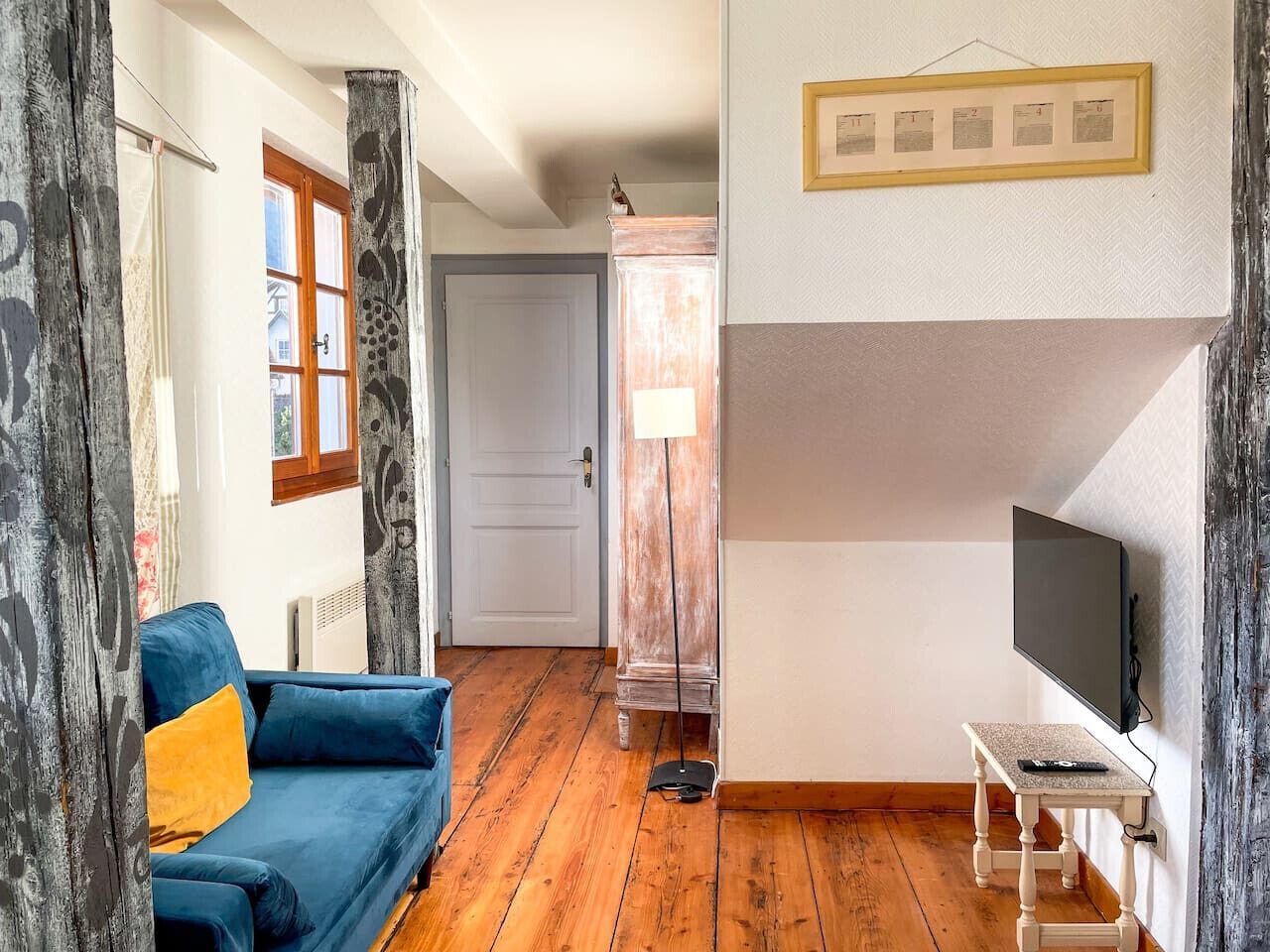 Een kamer met een blauwe bank, een televisie op een standaard, een houten vloer en een deur naar een andere kamer.