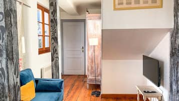Een kamer met een blauwe bank, een televisie op een standaard, een houten vloer en een deur naar een andere kamer.