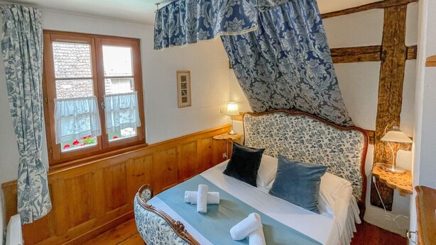 Een slaapkamer met een houten bedframe, een baldakijn en een raam met gordijnen.