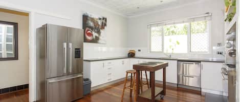 A modern kitchen with a stainless steel refrigerator, wooden stools, a window with a view, and a dishwasher.