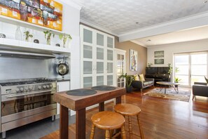 Een moderne keuken met een roestvrijstalen fornuis, witte kasten en een eethoek met een houten tafel en krukken.