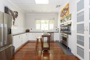 Een moderne keuken met witte kasten, roestvrijstalen apparatuur en een houten eettafel met krukken.