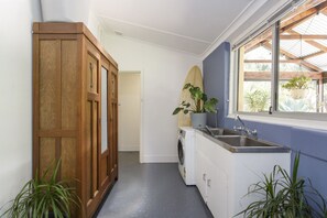 Eine schmale Küche mit Waschmaschine, Spüle und einem Fenster mit Blick auf Grünfläche.